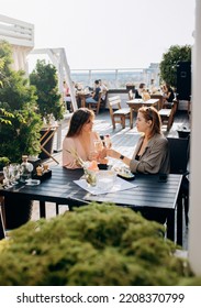 Two Women Friends Eating Fresh Oysters And Drinking Chilled Prosecco Wine On The Summer Sunset In Restaurant. Seafood Delicacies