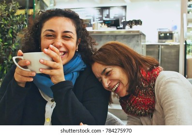 Two women friends enjoying a joke and a chat and a cup of coffee or tea, laughing and smiling in a cafe - Shutterstock ID 784275970
