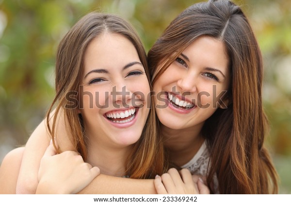 Two women friends laughing with a perfect\
white teeth with a green\
background