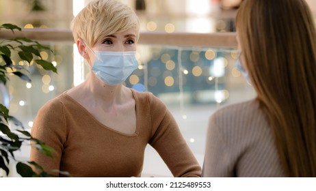 Two Women Friends Mother With Teenage Daughter Talking In Cafe Wear Medical Face Protective Masks. Adult 40s Woman Consultant Advise Client In Pandemic. Middle Aged Lady Talking To Unrecognizable Girl