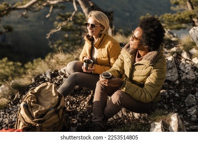 Two women friends in nature enjoying a coffee break during a hike in the mountains. - Powered by Shutterstock