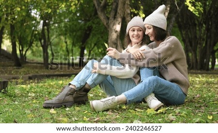 Two women friends or sisters hugging outdoors in autumn park