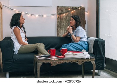 Two Women Friends Talking To Each Other On A Couch In Apartment