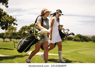 Two women golfers smile as they walk across a vibrant golf course, carrying their bags during a lively team competition. Enjoyment of outdoor sports together. - Powered by Shutterstock