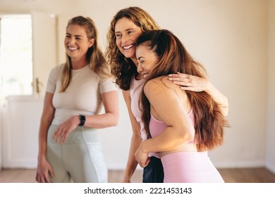 Two women greeting each other with a hug in a yoga studio. Happy female friends attending a yoga class in a community wellness centre. Women of different ages starting a fitness session. - Powered by Shutterstock