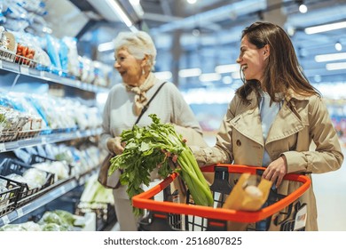 Two women happily browse fresh produce in a supermarket, enjoying their grocery shopping experience. They carry a basket filled with vegetables, showcasing healthy lifestyle choices. - Powered by Shutterstock