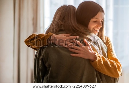 Two women happily gently hugging, a young girl smiles and hugs her friend, has a good time with a relative or celebrates a holiday, rejoices at a meeting, feeling love and emotional bonding.