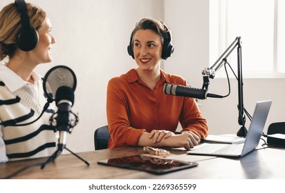 두 여성이 홈 스튜디오에서 오디오 방송을 공동 진행하면서 대화를 하고 있습니다. 두 명의 여성 콘텐츠 제작자들이 그들의 소셜 미디어 채널을 위해 인터넷 팟캐스트를 녹음하고 있다. 스톡 사진