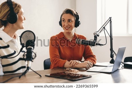 Two women having a conversation while co-hosting an audio broadcast in a home studio. Two female content creators recording an internet podcast for their social media channel.