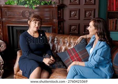 Two women having a therapy session in a classic library interior. A professional psychologist in a blue suit listens to her client. Concept of mental health, support, and professional counseling.