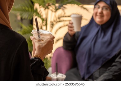 Two women in hijabs enjoy coffee and conversation at a cozy café, creating a warm and friendly atmosphere. The focus is on their drinks and hands, symbolizing connection and community. - Powered by Shutterstock