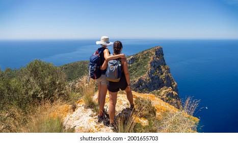 Two Women Hikers On Mountain Summit Overlooking The Mediterranean Sea. Outdoor Adventure Day Trek With A Friend.