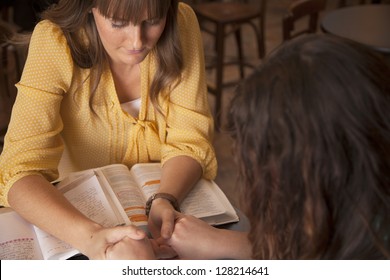 Two Women Hold Hands And Pray As They Study The Bible.