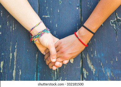 Two Women Holding Hands With A Wooden Background. One Is Caucasian, The Other Is Black. Multicultural, Homosexual Love And Friendship Concepts.