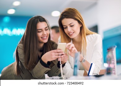 Two Women Is Holding A Mobile Phone In Store. They Are Looking For New Smart Phone.