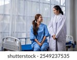 Two women in hospital gowns are smiling at each other. One of them is a nurse and the other is a patient