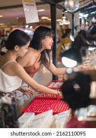 Two women inquiring about fashionable accessories and jewelries as well as haggling the prices at a booth inside a shopping mall.