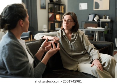 Two women are intently discussing mental health in a counseling session Both are seated on a comfortable couch in a cozy, well-decorated room surrounded by books and personal items - Powered by Shutterstock