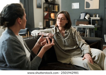 Two women are intently discussing mental health in a counseling session Both are seated on a comfortable couch in a cozy, well-decorated room surrounded by books and personal items