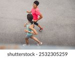 Two women jogging together on a paved surface, one in a pink shirt and the other in a light blue tank top. They appear to be enjoying their exercise routine.