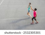 Two women jogging together on a sports court, one in a light blue tank top and shorts, the other in a pink shirt and black leggings. They appear to be enjoying their exercise routine.