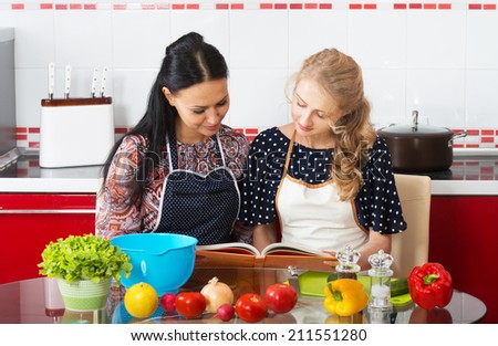 Two women in the kitchen cook using cookbook