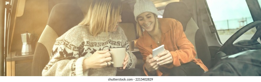 Two Women Laughing Looking Mobile With A Cup Of Coffee Sitting In The Front Seat Of A Camper Van