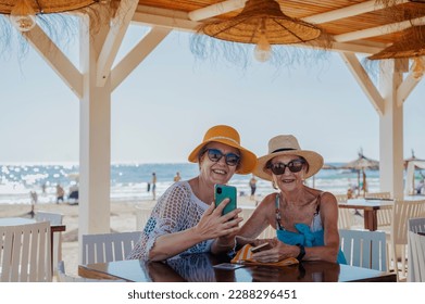 Two women laughing with a smartphone in a beach bar. - Powered by Shutterstock