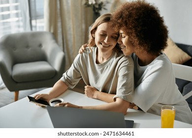 Two women, a lesbian couple, cuddle while using a laptop and enjoying a beverage. - Powered by Shutterstock