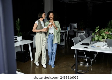 Two women, a lesbian couple, laugh together in an office setting while holding coffee cups. - Powered by Shutterstock