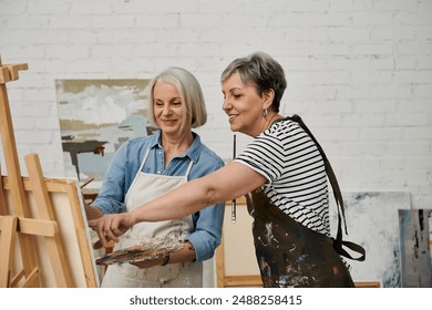 Two women, a lesbian couple, are painting together in an art studio. One woman is guiding the other hand as she holds a paintbrush. - Powered by Shutterstock