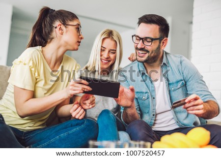 Two women and a man in living room holding credit card and digital tablet