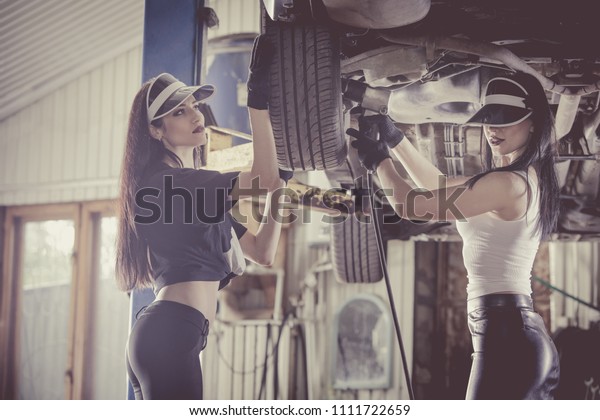 Two\
women mechanics are repairing a car on the\
lift.