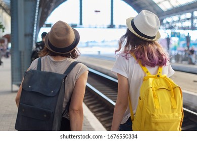 Two women mother and teenage daughter walking with luggage at railway station. People awaiting the arrival of trains, back view - Powered by Shutterstock