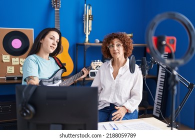 Two Women Musicians Having Online Electrical Guitar Lesson By Smartphone At Music Studio