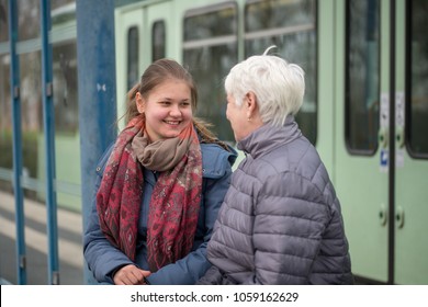 two women, old and young,  sit on the bench at tram stop
