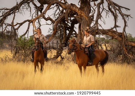 Two women on horseback by dead tree