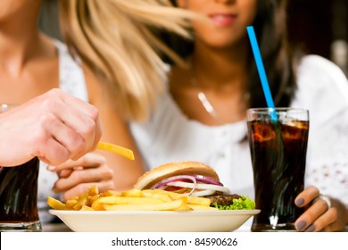 Two Women - One Is African American - Eating Hamburger And Drinking Soda In A Fast Food Diner; Focus On The Meal