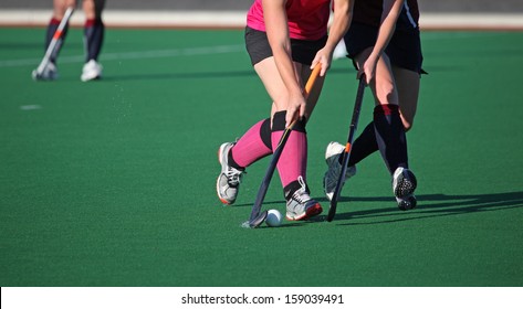 Two women players contest for the ball in a game of field hockey