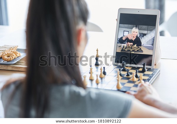 Two women playing chess in video chat online on laptop computer at home