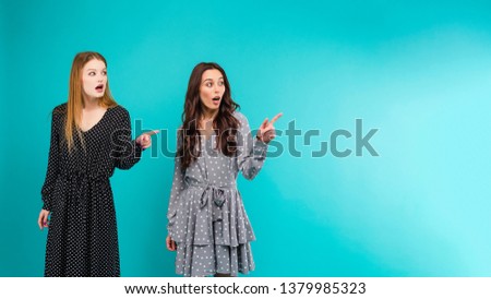 two women pointing at copy space isolated over blue turquoise background