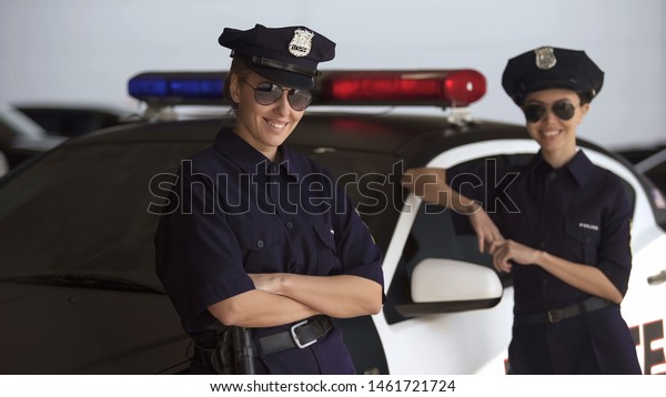 Two women in police uniforms standing near\
patrol car and smiling, law and\
order