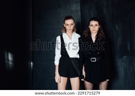 two women pose on black background