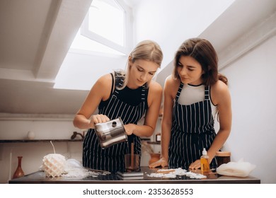 Two women pour wax into a mold for a candle.