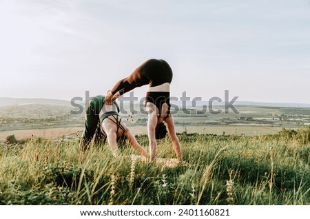Two women practicing acroyoga on a hill at sunset