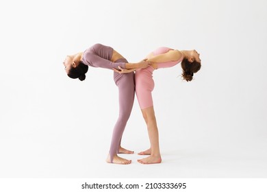 Two women practicing yoga, holding hands and performing the Hasta Uttanasana exercise, backbend, stand on a white background.