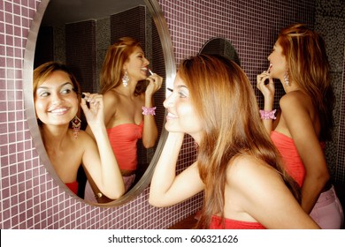 Two Women In Public Restroom, Looking At Mirror, Applying Make-up