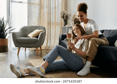 Two women relax at home, one sitting on the floor and the other on a couch, looking at a phone together. - Powered by Shutterstock