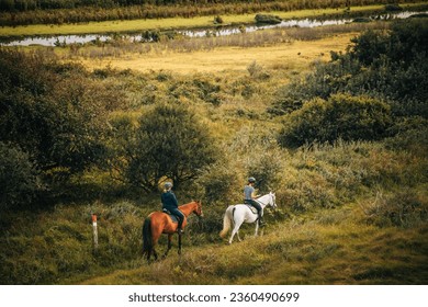 Two women riding a brown and white horse along a trail through a swampy oceanside landscape with small ponds and a river  - Powered by Shutterstock