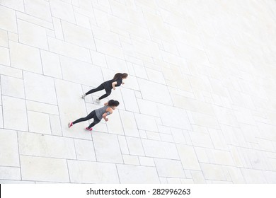 Two Women Running In The City, Aerial View. They Are Wearing Gray And Black Sportswear.